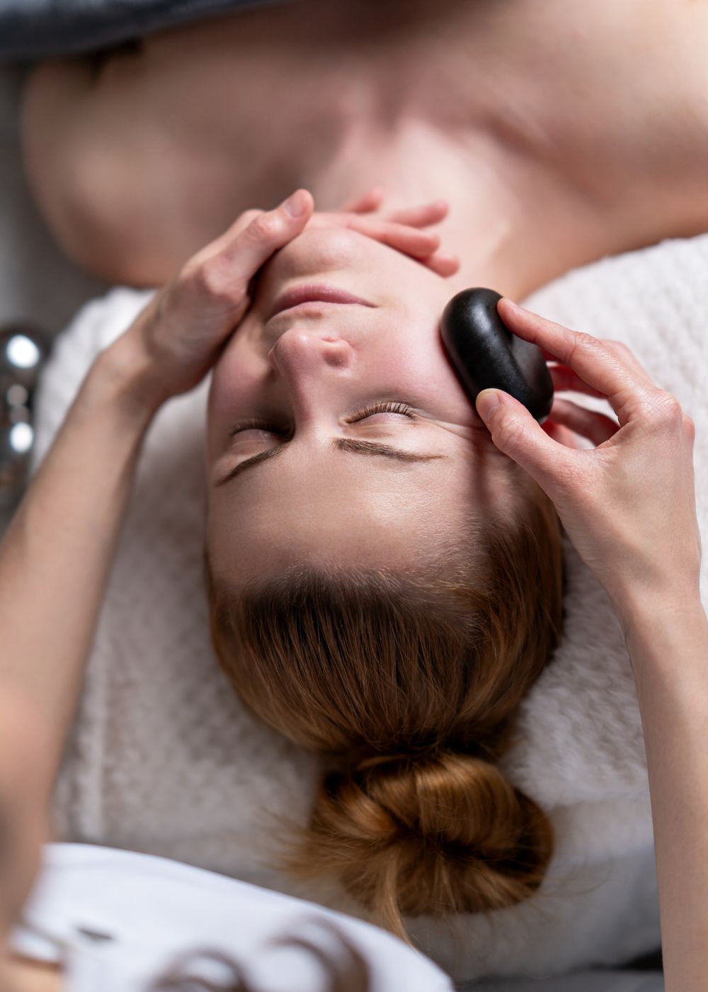 Close-up of spa facial treatment using black hot stones in professional setting.