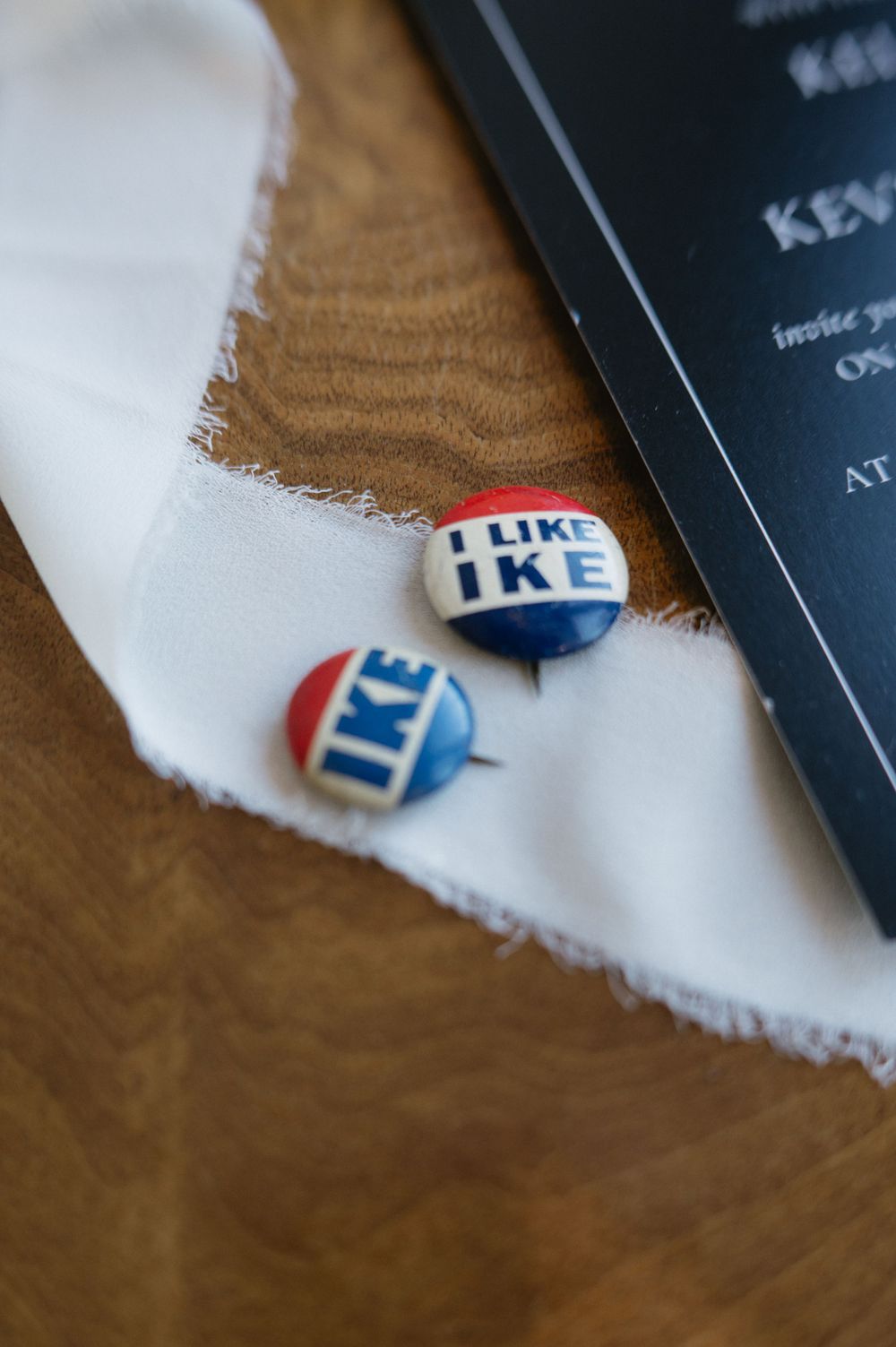 Vintage 'I Like Ike' campaign buttons on a white cloth against a wooden surface.