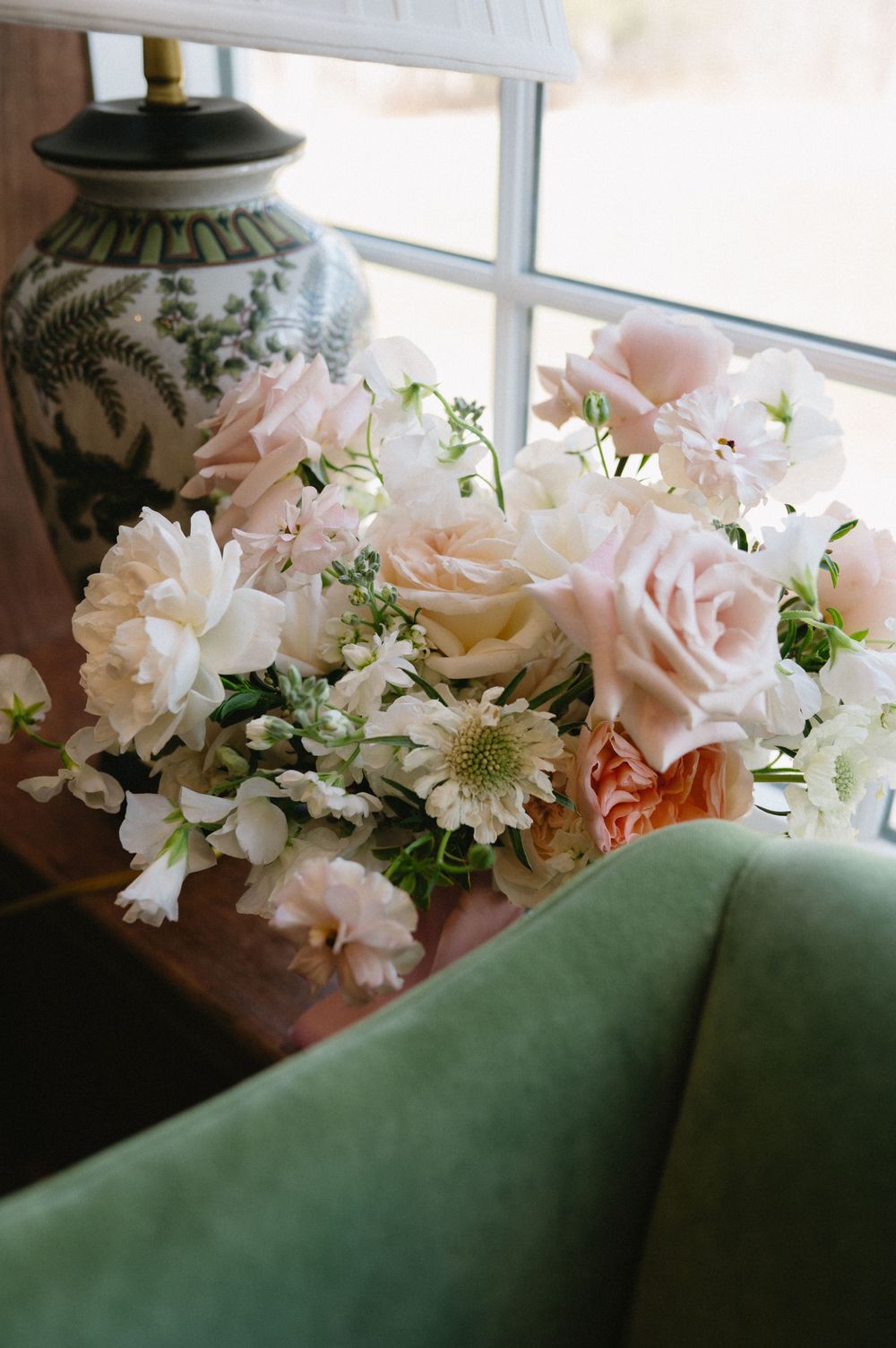 Delicate pink and white flower arrangement next to a decorative vase by a window.
