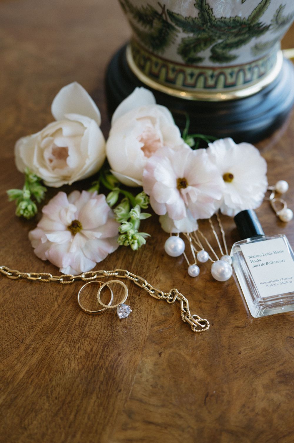 Wedding accessories including rings, pearls, and pale pink flowers on a wooden surface.