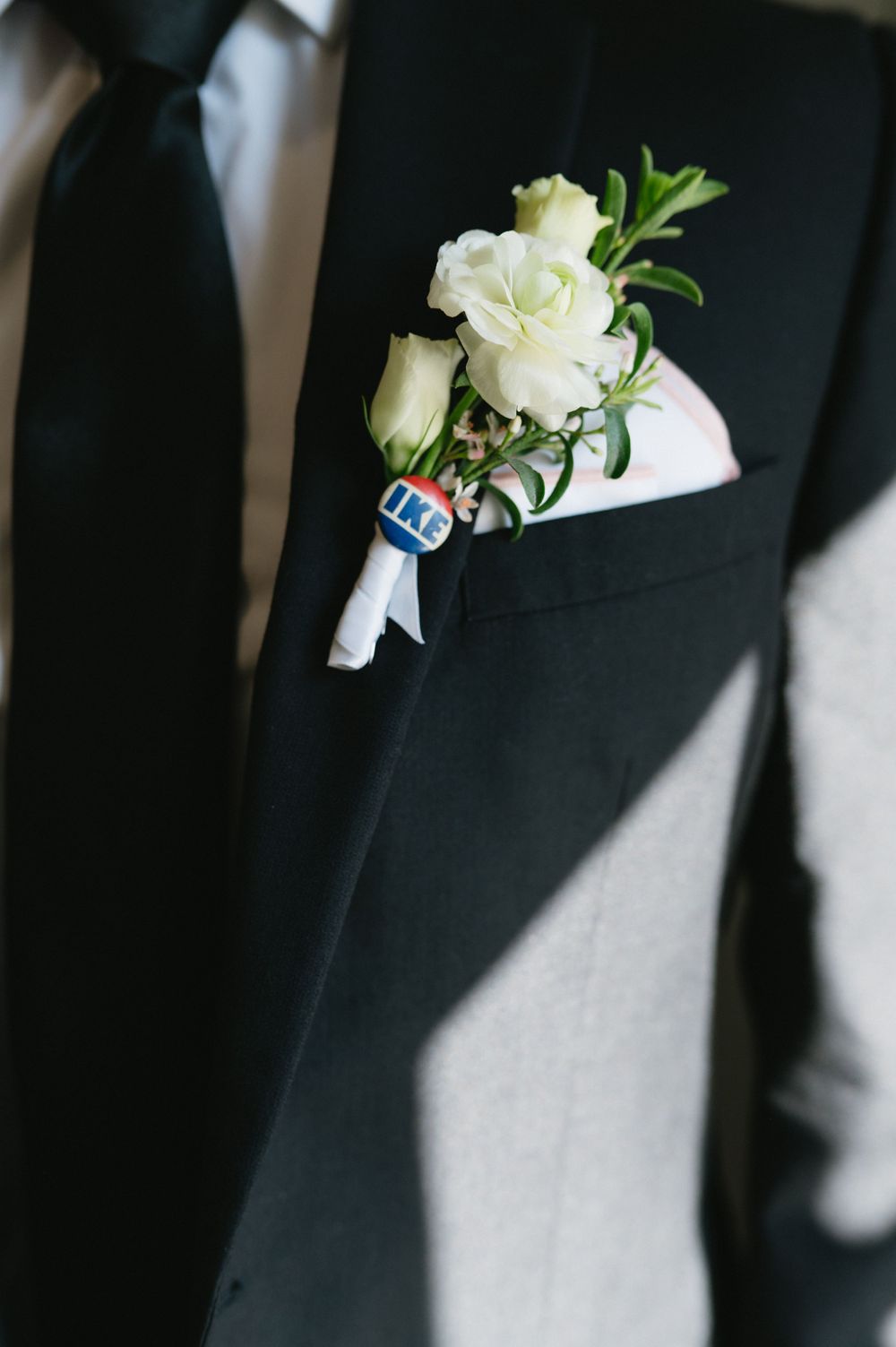 White rose boutonniere with 'IKE' pin attached to black suit lapel.