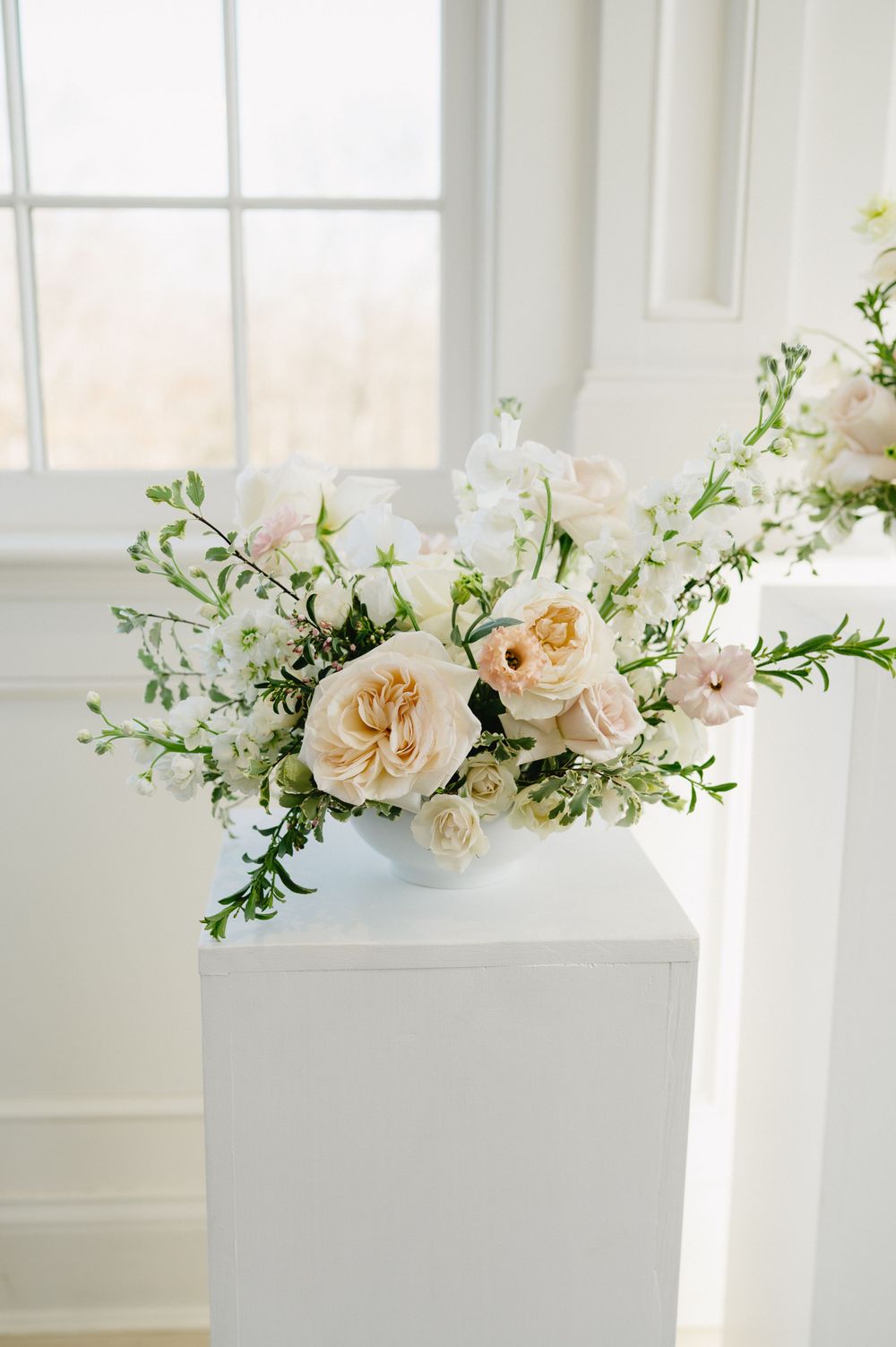 Elegant floral arrangement with roses and greenery on white pedestal.