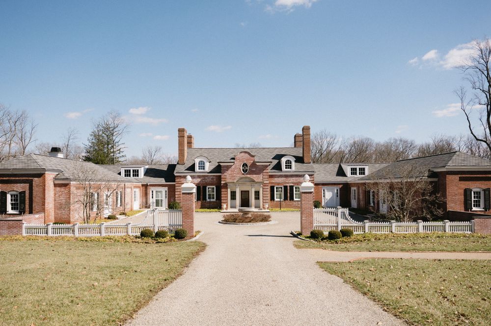 A grand brick estate with colonial architecture and manicured grounds on a sunny day.