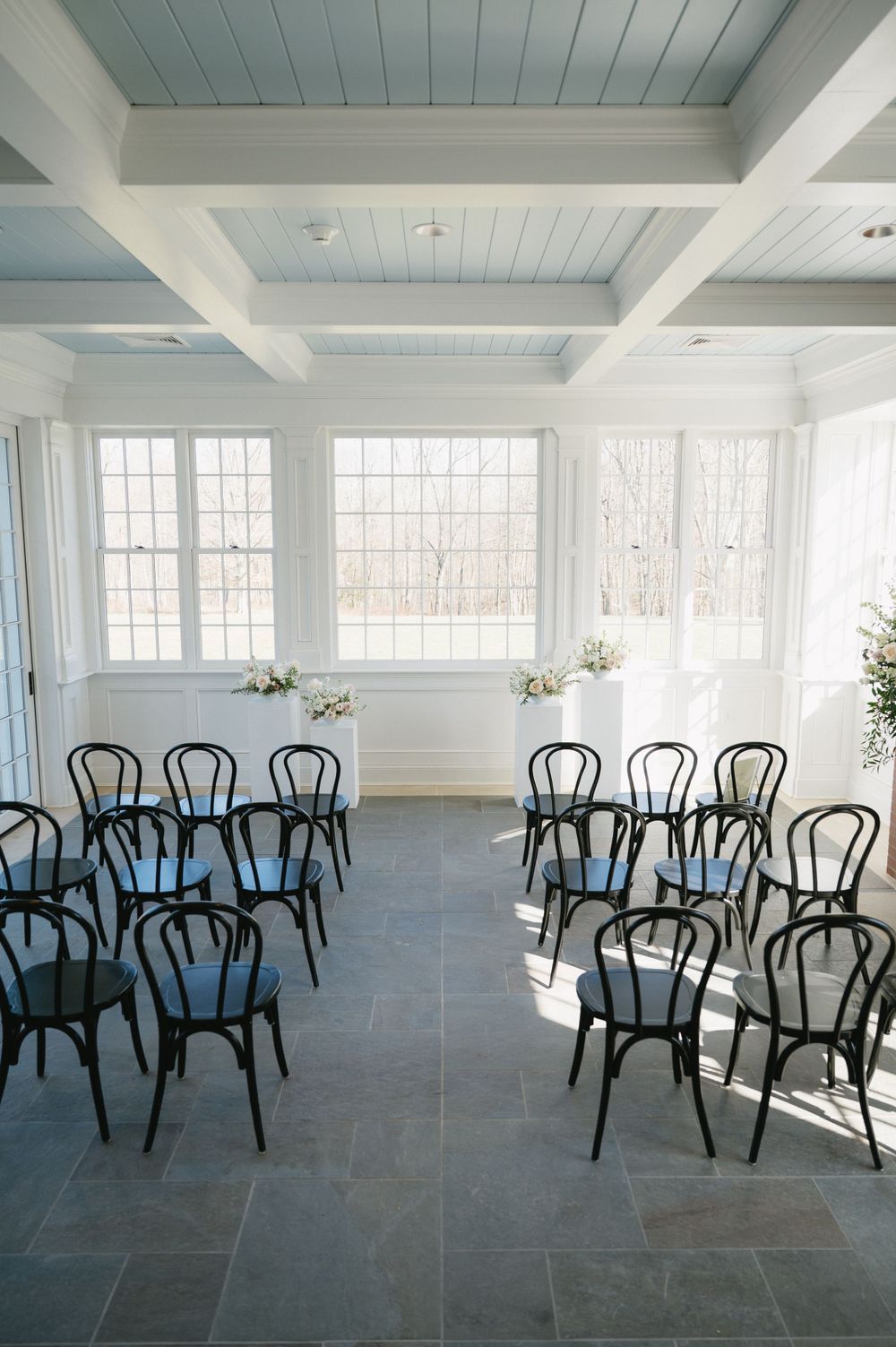 An elegant wedding ceremony space with black bentwood chairs and coffered ceiling.