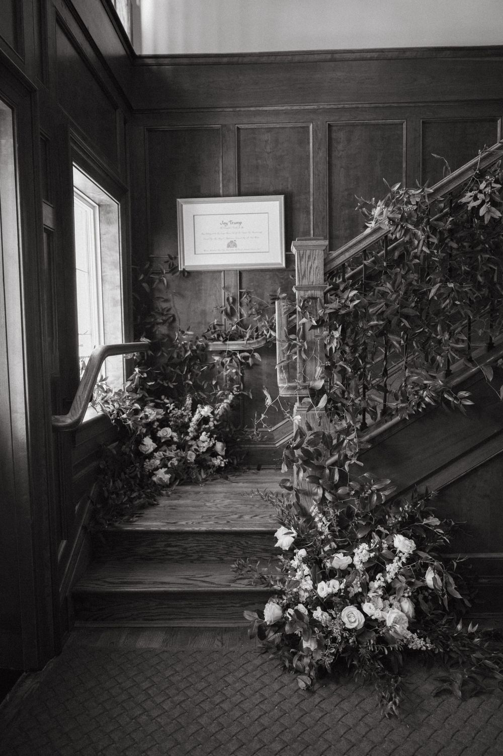 A dramatic black and white photo of floral arrangements decorating an ornate staircase.