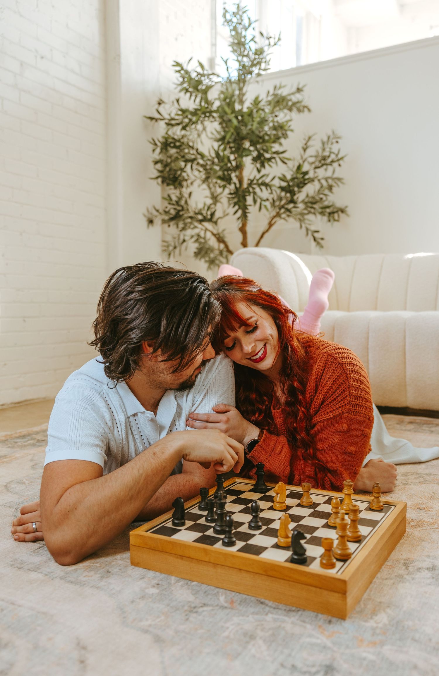 A playful couple enjoys a game of chess on a living room floor.