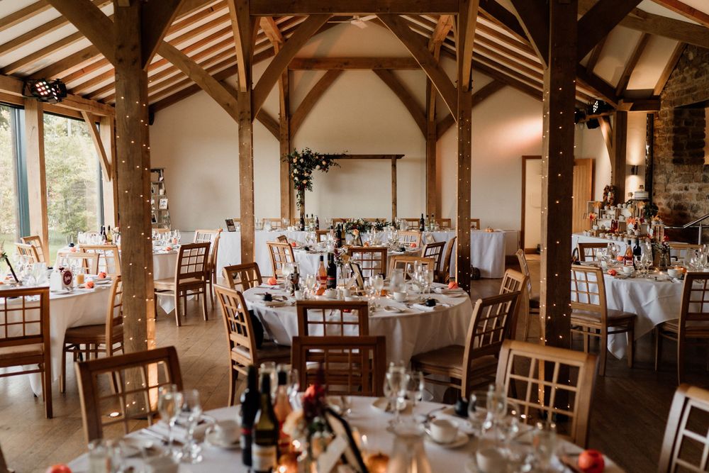 Elegant rustic wedding reception venue at Dodford Manor Barns with wooden beams and decorated round tables.