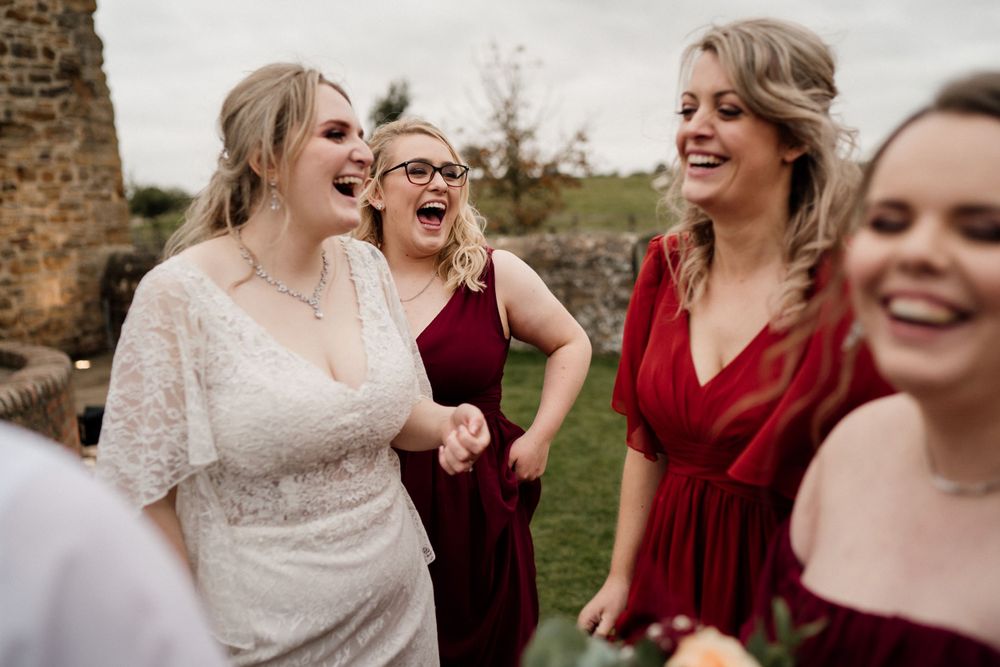 A joyful candid moment at a wedding celebration with laughter and burgundy dresses.