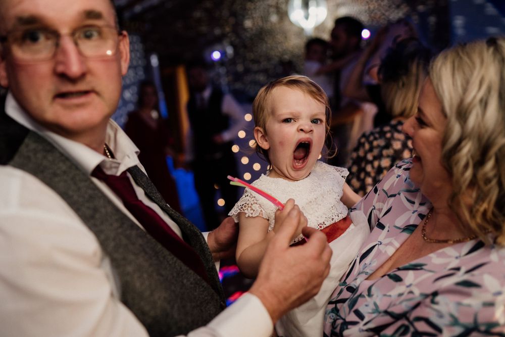 A yawning baby in white dress attends a wedding celebration.