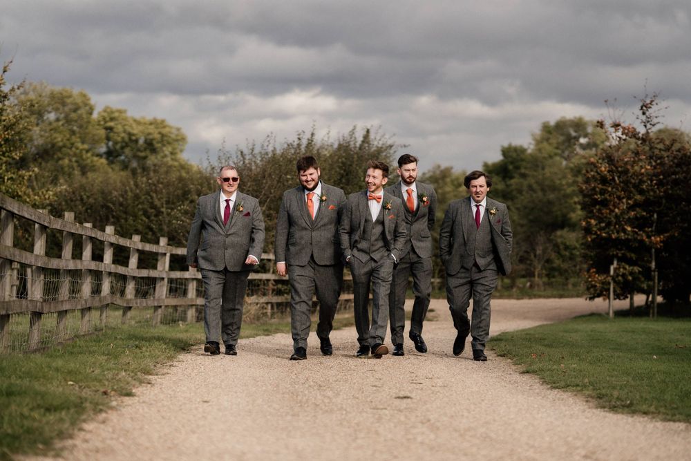 Groomsmen in gray suits walking together on a countryside path at Dodford Manor.