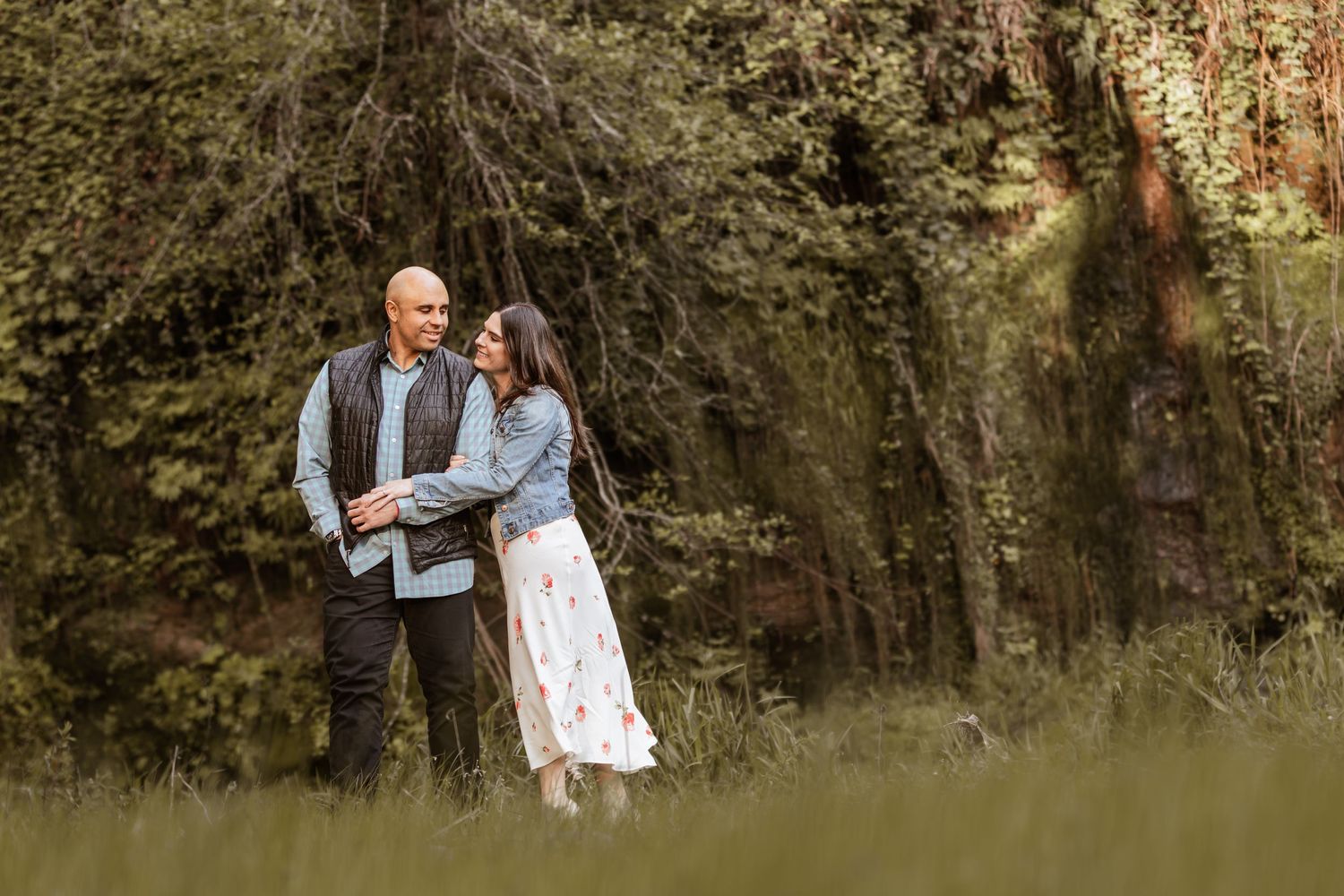 A couple shares an intimate moment while standing together in a lush natural setting during golden hour.