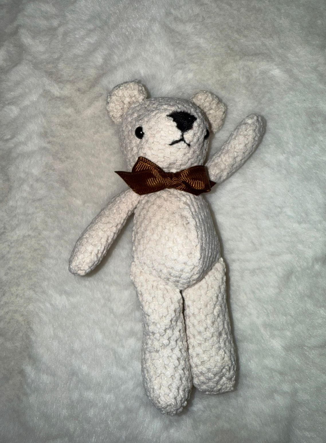 A white knitted teddy bear with brown bow tie shown in various poses on gray background.