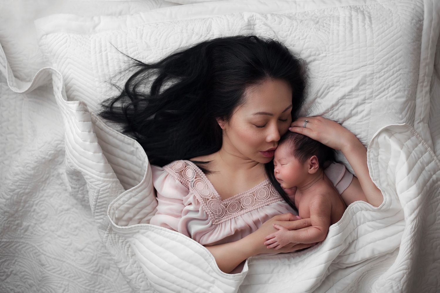 Mother lovingly cuddles her newborn baby in bed, both peacefully asleep, wrapped in soft white blankets and warm, tender affection.
