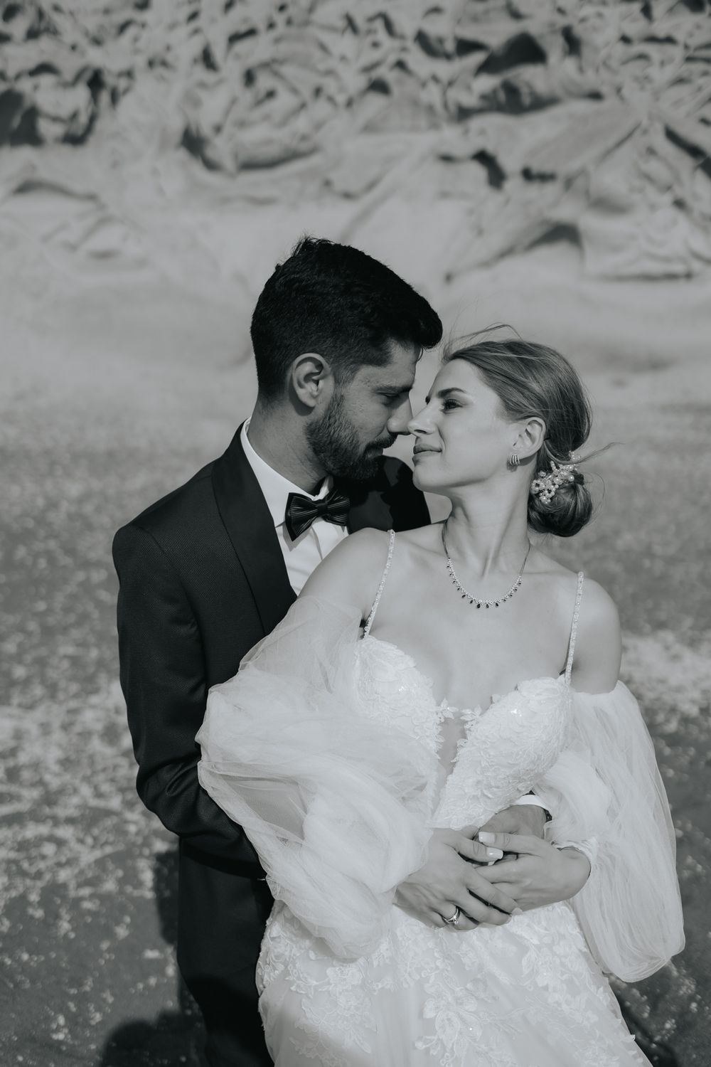 Romantic black and white portrait of newlyweds in formal attire embracing outdoors.