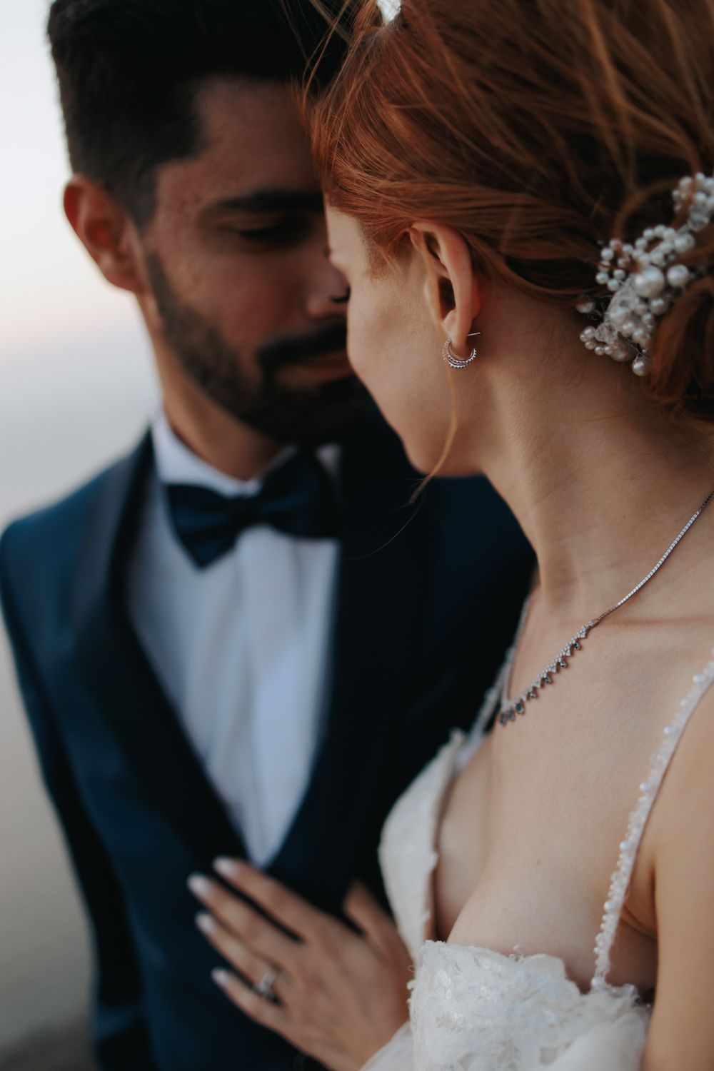 Romantic wedding portrait showing elegant couple in navy tuxedo and white dress with pearl hair accessories.