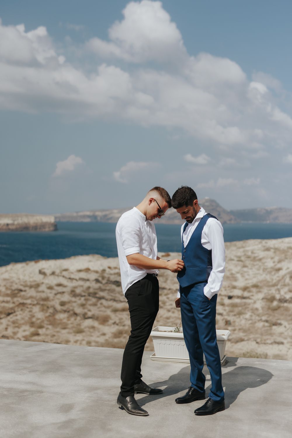 Two people sharing an intimate moment on a clifftop overlooking a beautiful blue sea and coastline on a sunny day.