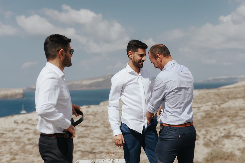 Three people in white shirts having a conversation while standing on a hillside overlooking coastal waters.