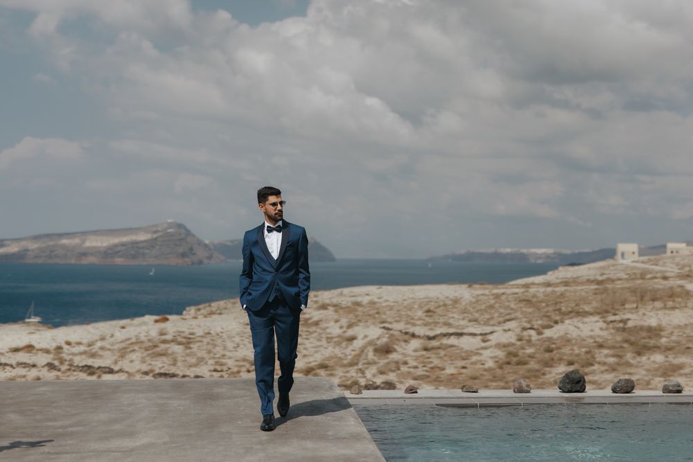 A person in a navy blue suit walks along a seaside path with rocky cliffs and ocean views in the background.