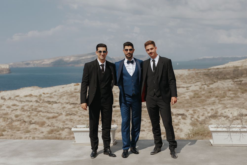 Three well-dressed men stand together against a scenic mountain landscape backdrop.