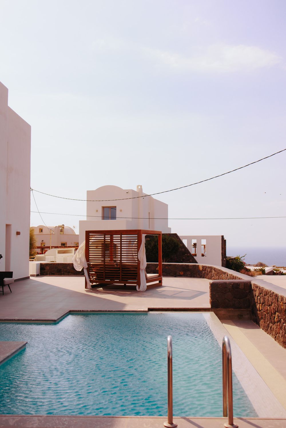 Modern Mediterranean villa with pool and wooden cabana on rooftop terrace overlooking scenic coastal landscape.