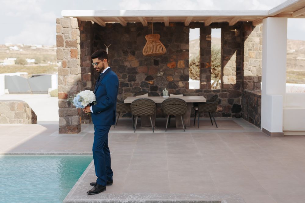 A person in a blue suit stands near a swimming pool at a covered outdoor dining area.
