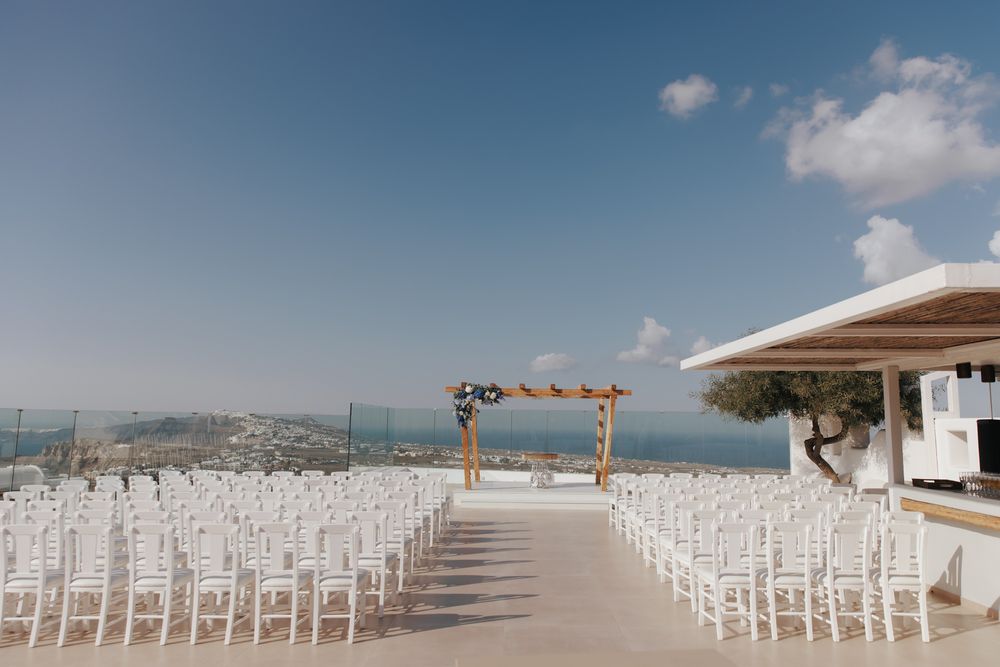 White chairs arranged under a wooden arch for an outdoor wedding ceremony overlooking a scenic coastal landscape.