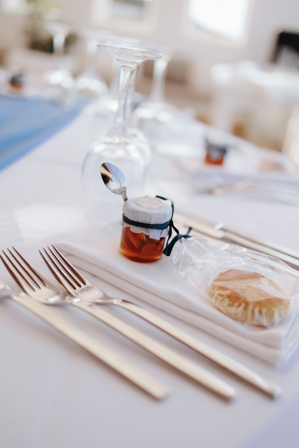 Table place setting with elegant silverware, an upturned wine glass, and small jars of condiments on a white tablecloth.