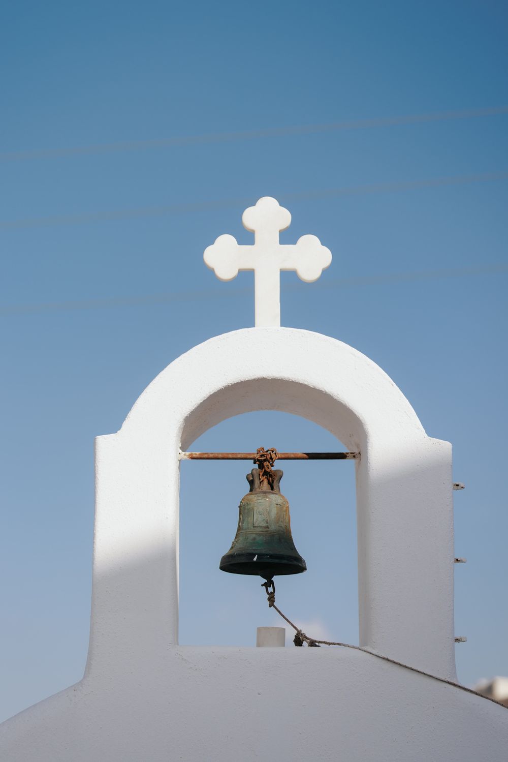 A white church bell tower with a cross on top against a clear blue sky in Mediterranean architecture style.