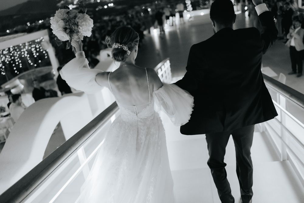 Black and white photo of a lively wedding reception scene with people dancing and spinning on a reflective dance floor.