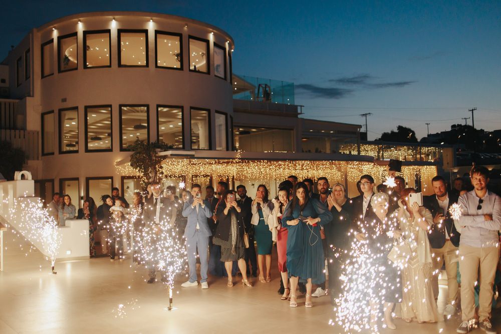 Crowd gathered outside illuminated building at dusk with sparklers creating a festive atmosphere.