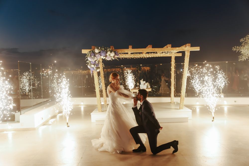 A romantic moment with sparklers and string lights under a wooden pergola during an evening celebration.