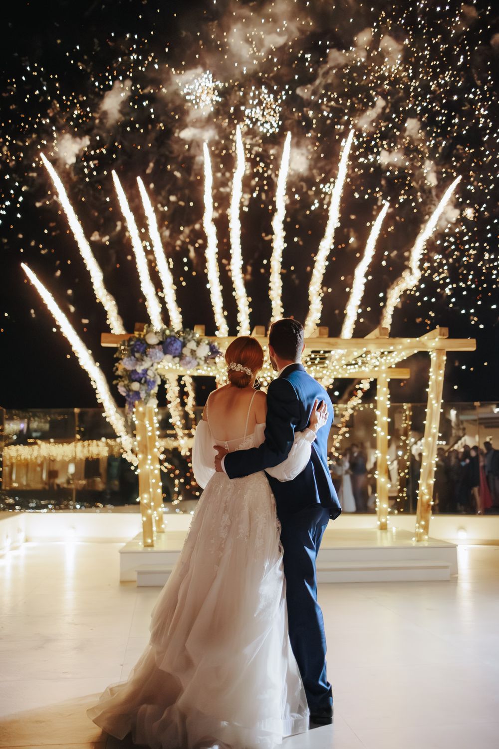 Couple embraces on dance floor while dramatic firework effects create magical backdrop during celebration.