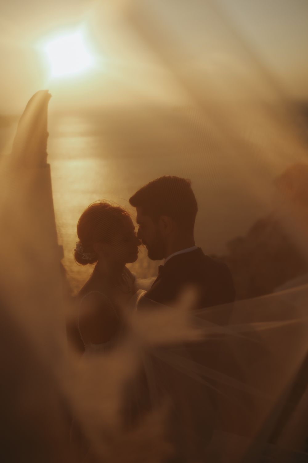 Two silhouettes in romantic embrace against soft sepia light creating dreamy atmosphere in vintage style photograph.