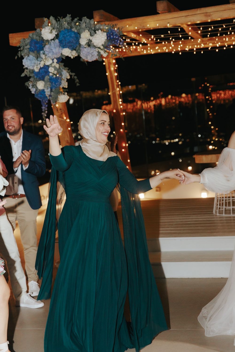 A person in an elegant emerald green flowing dress dances under a floral-decorated pergola with string lights.