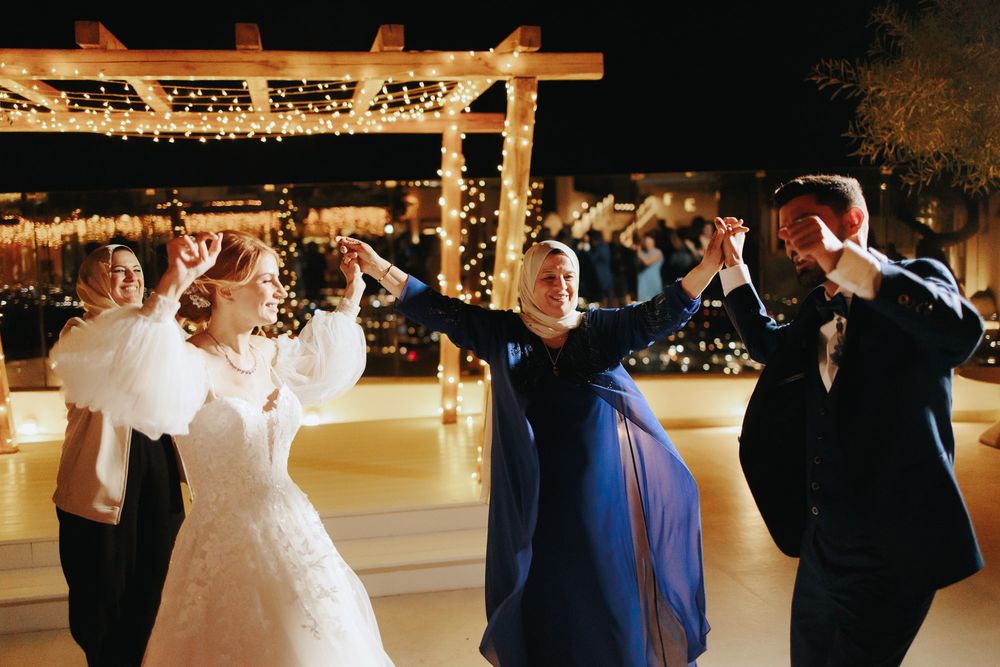 People dance and celebrate at an evening wedding reception under string lights on an outdoor dance floor.