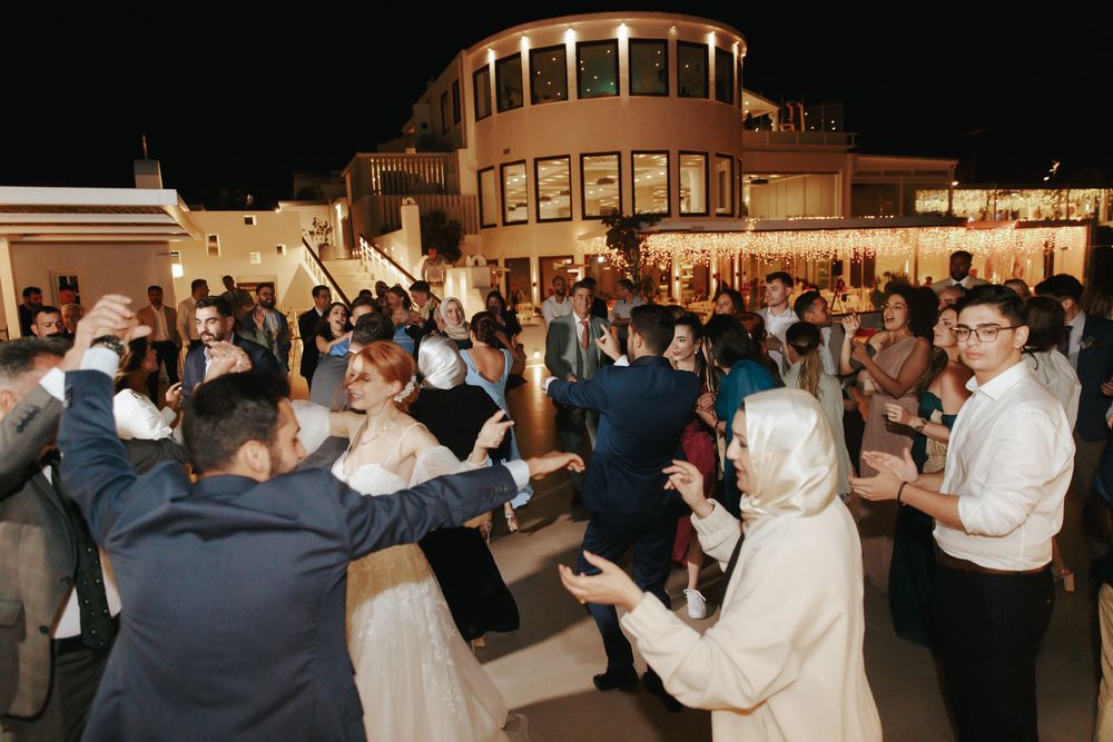 Nighttime celebration with crowd of partygoers dancing outside an illuminated building with domed architecture.