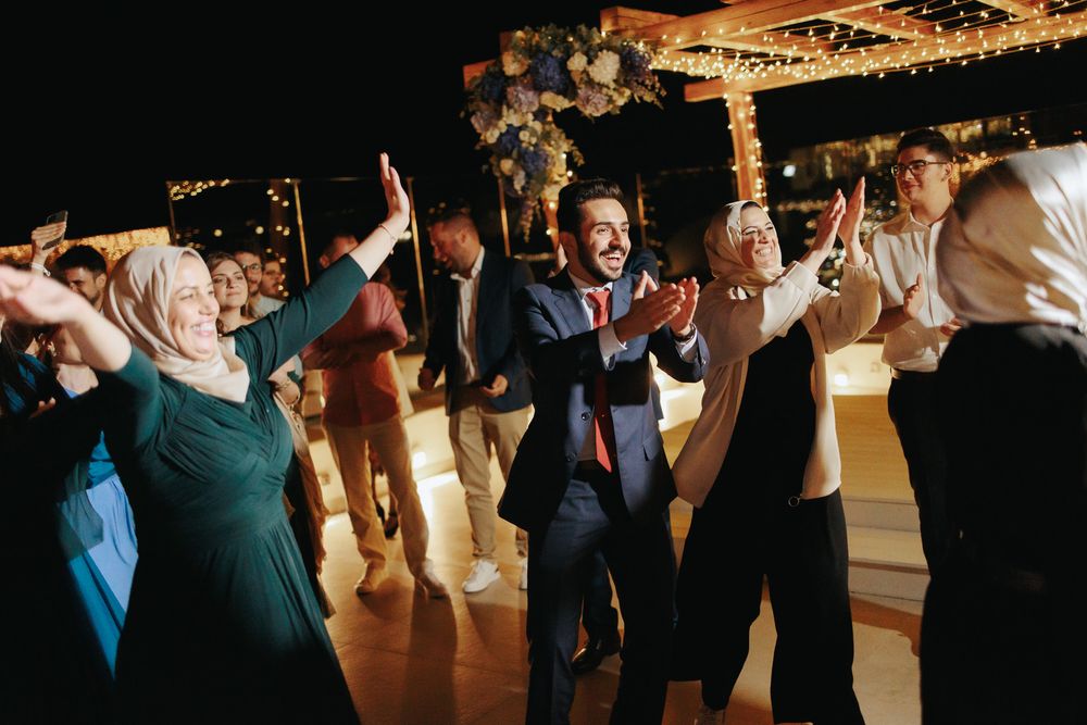 Wedding guests dancing enthusiastically with raised arms during an evening reception celebration.
