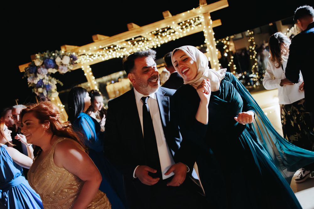 Wedding guests having fun dancing and celebrating under decorative lighting at an outdoor evening reception.