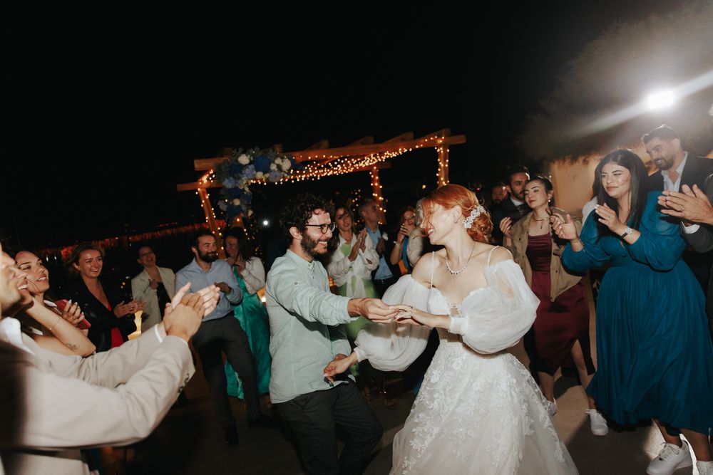 People dancing joyfully at a nighttime wedding reception under string lights on an outdoor dance floor.