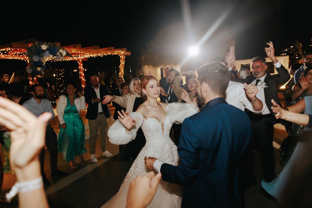 Wedding party dancing enthusiastically under illuminated pergola during outdoor evening celebration.