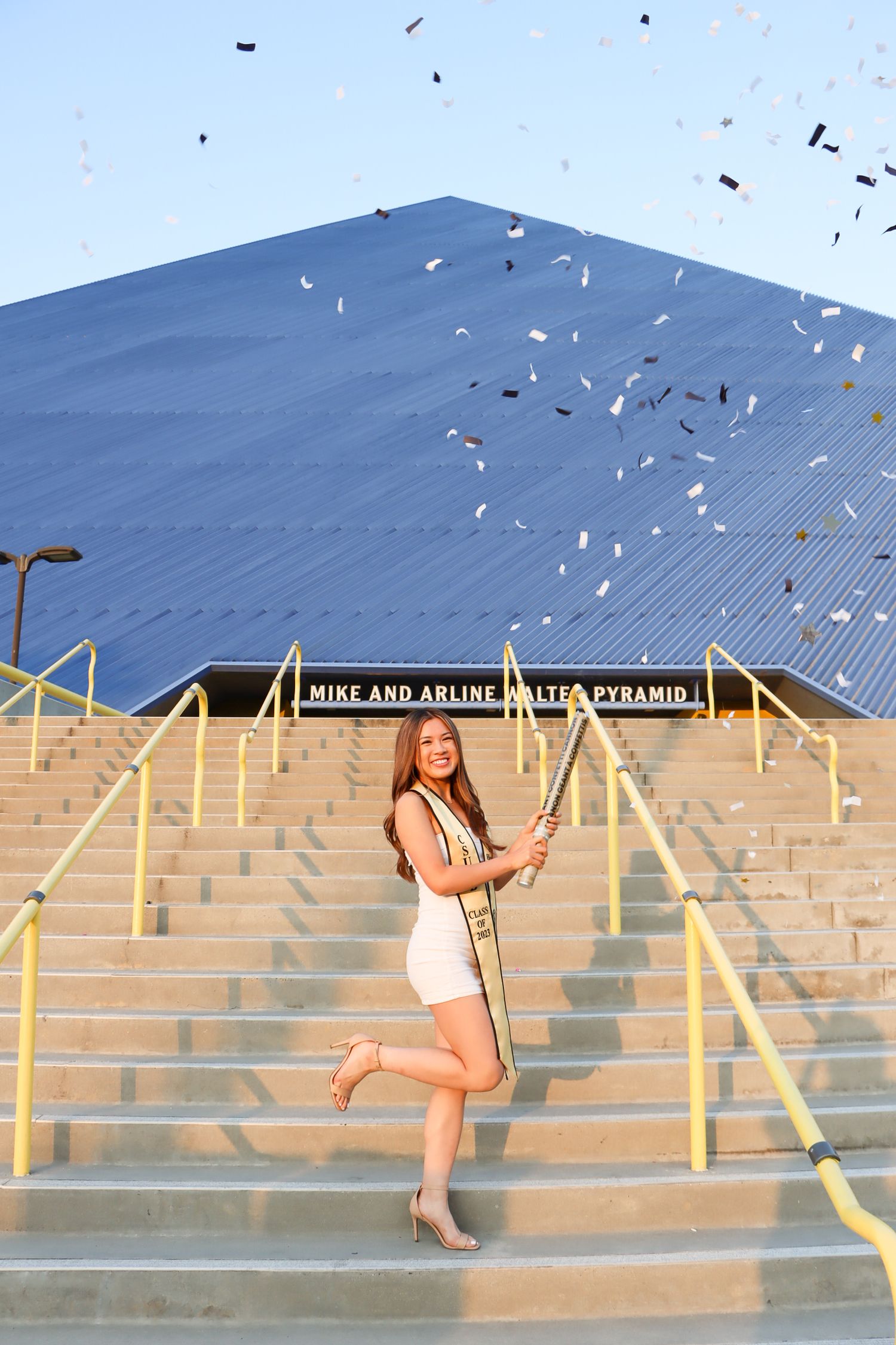 Graduate tossing confetti on campus steps while holding diploma and wearing graduation regalia.