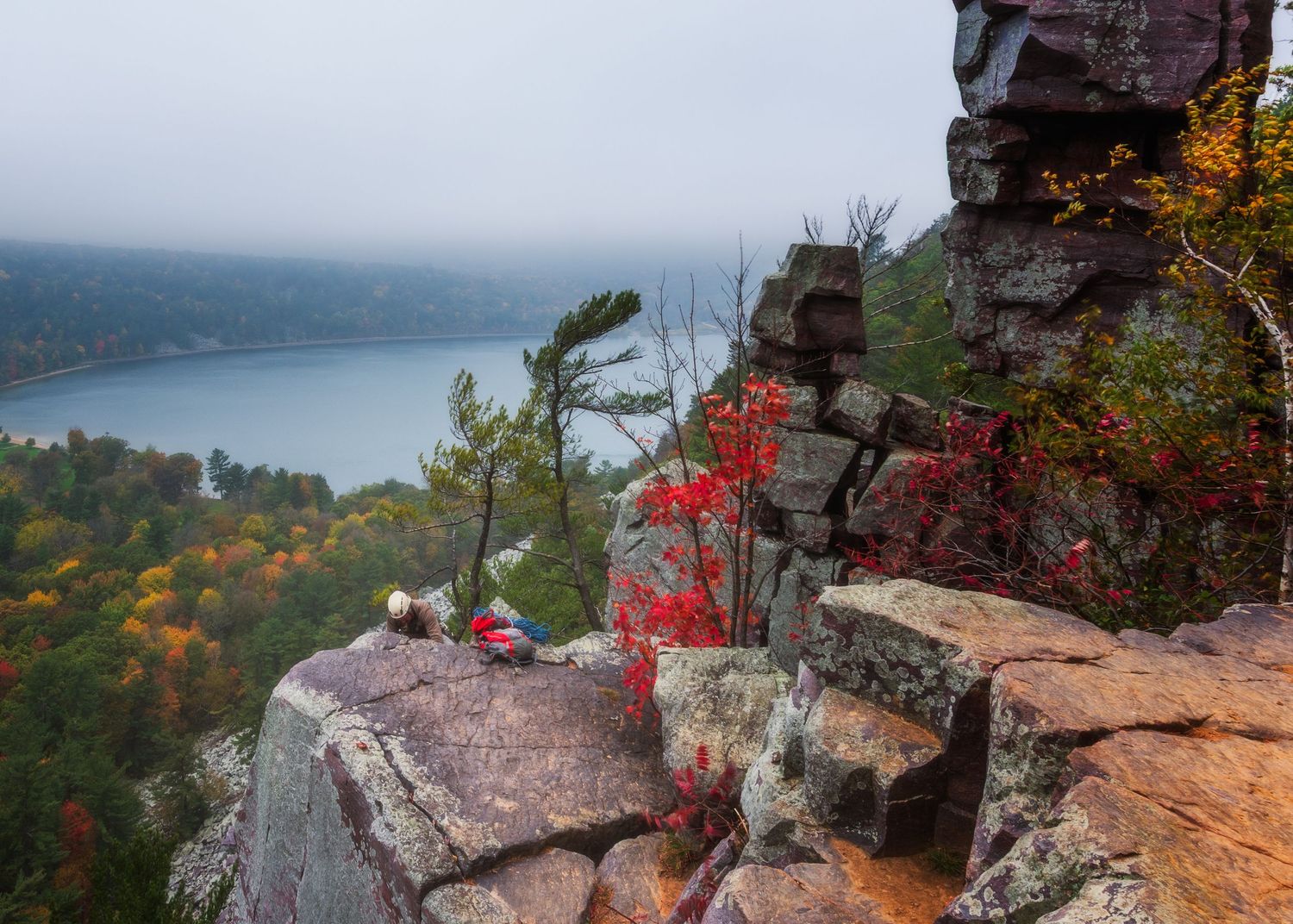 Autumn foliage and rocky cliff overlooking misty lake landscape.