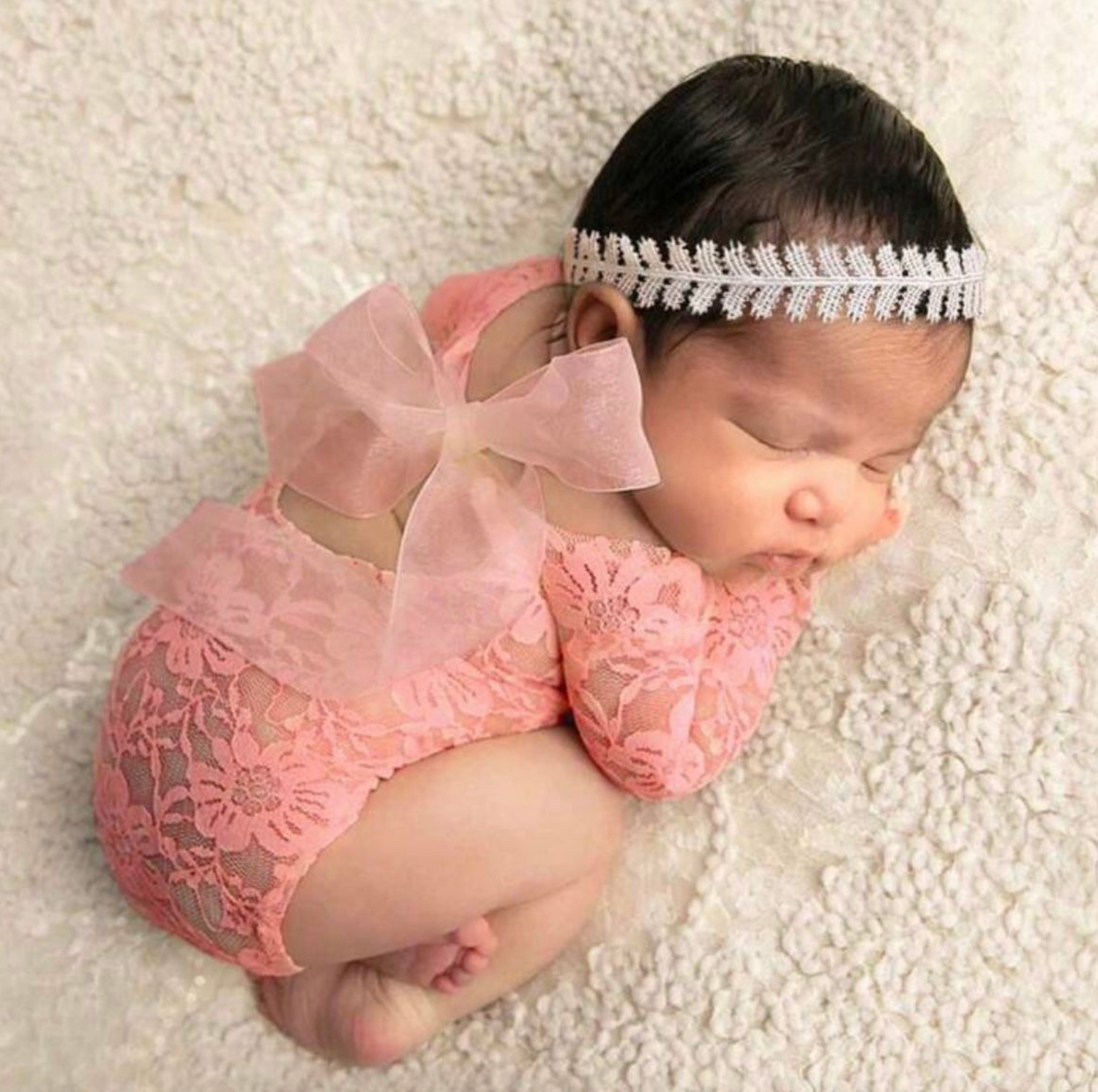 Newborn photography setup with pink lace outfit on cream textured background.