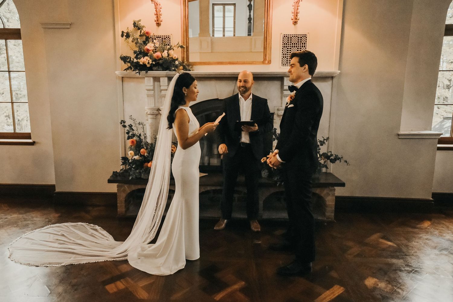 Intimate wedding ceremony inside a historic chapel with romantic light streaming through arched windows during indoor gathering.