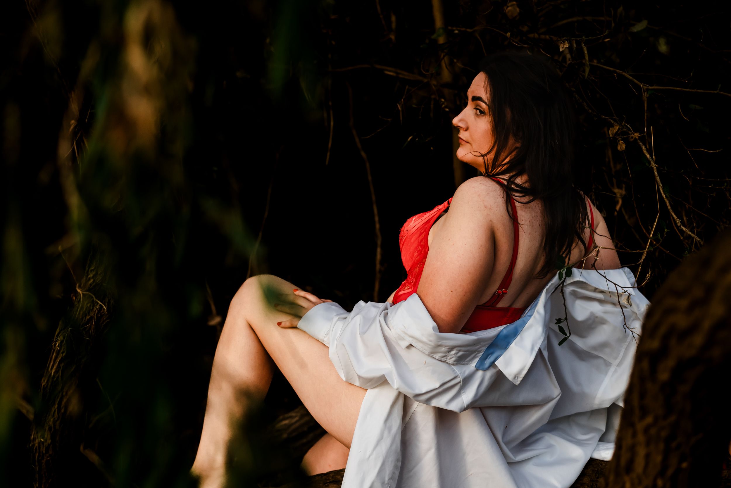 Figure wearing red top and white robe poses gracefully in moody outdoor forest setting.