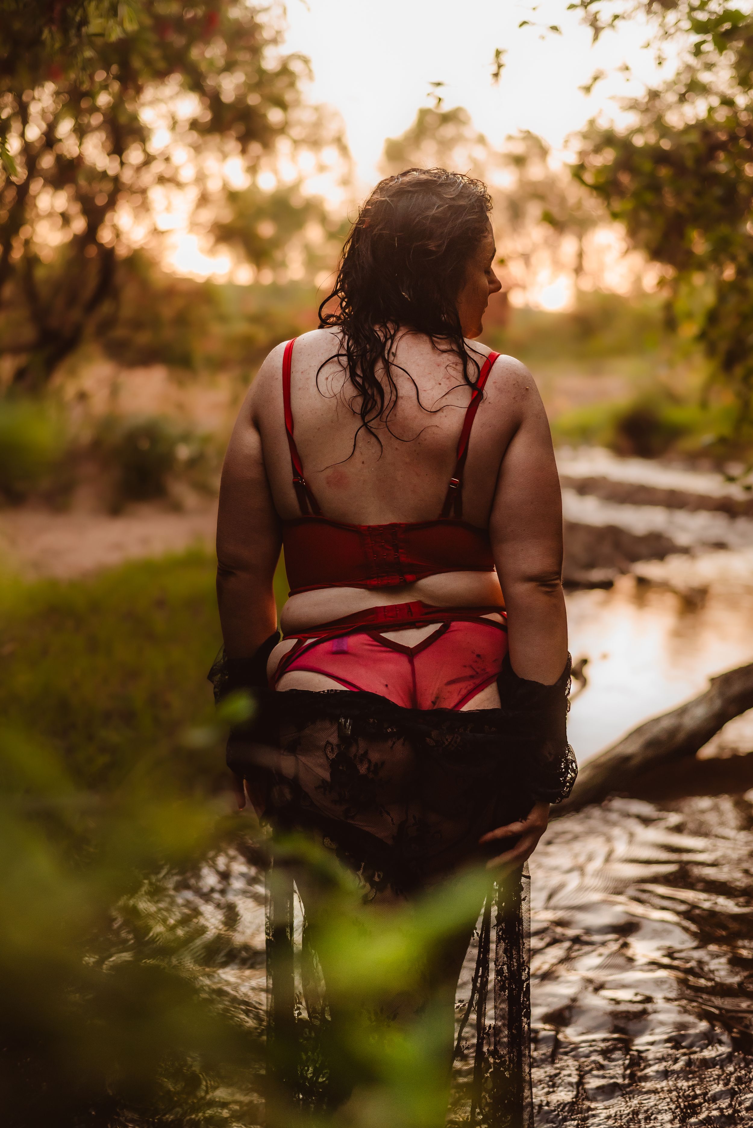 Sensual outdoor boudoir session near water at sunset with red attire.
