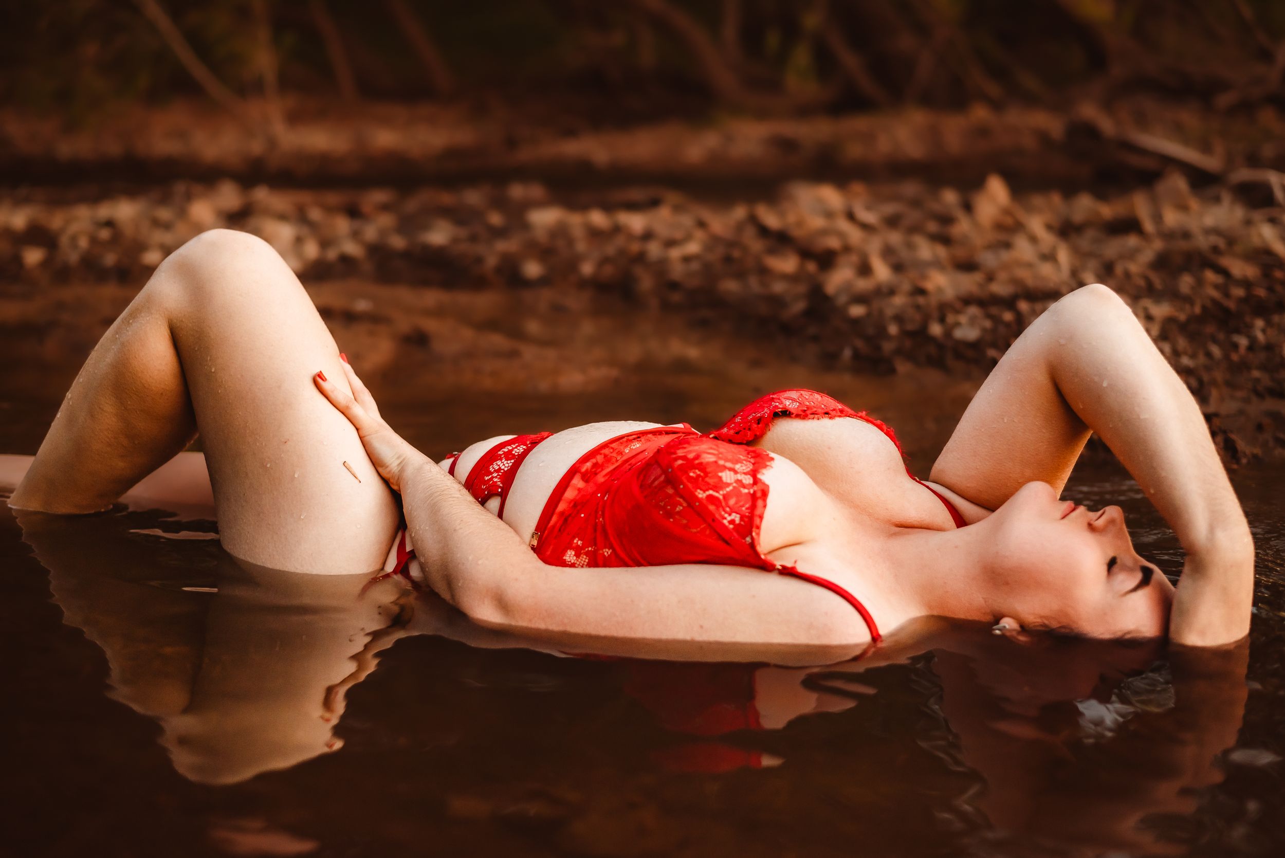Artistic boudoir photography with red lingerie in dark moody lighting.