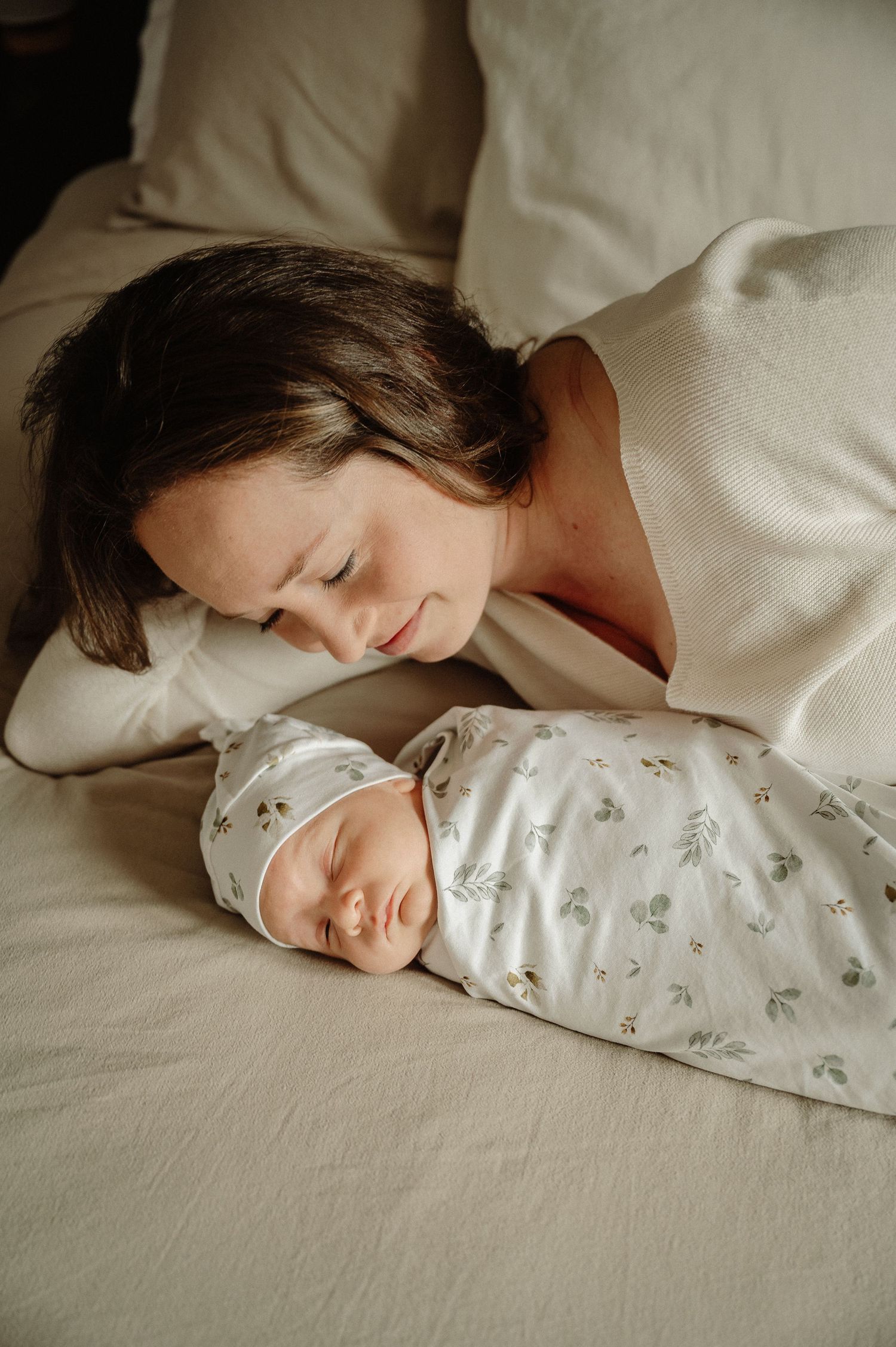 A peaceful moment of mother and sleeping newborn baby cuddling together in bed.