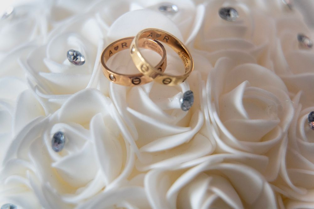 Two gold wedding bands resting on white satin roses decorated with rhinestone accents.