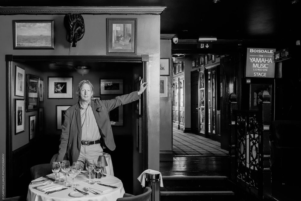 A black and white photograph shows a person in a restaurant interior with wood paneled walls and vintage decor.